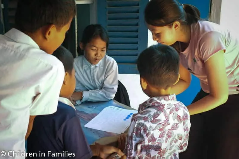 CIF social worker and 4 children fill in paperwork as part of community